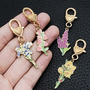 Set mit vier Blumen-Emaille-Schlüsselanhängern mit goldenen Herz-Haken auf Lederhintergrund