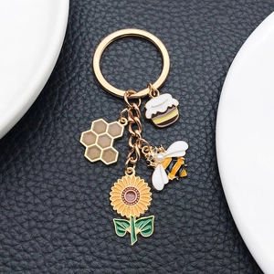 Detail of bee and sunflower enamel charms on gold keychain over black leather