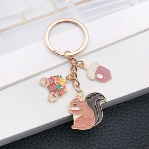 Detail view of squirrel, acorn and pumpkin cart charms on a gold tone metal keychain