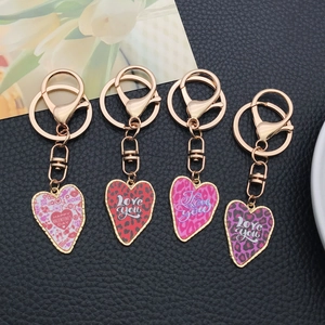 Set of four leopard print heart keychains with gold metal rings on black leather background