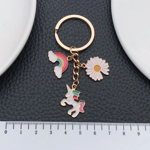 Golden unicorn keychain with rainbow and daisy enamel charms on black leather background