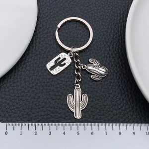 Antique silver desert cactus keychain charms on black leather background with ruler