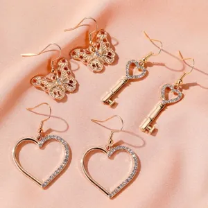 Detail view of gold butterfly, heart, and key earring set on elegant satin background