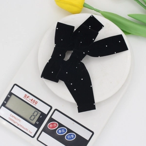 Pair of black velvet bow hair clips with white polka dots shown on a scale for weight