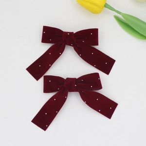 Pair of burgundy velvet bow hair clips with rhinestones on a white background