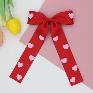 Detailed view of red satin bow hair clip with pink heart embroidery and long ribbons