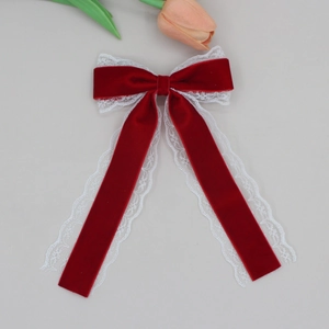 Detail of burgundy velvet ribbon bow hair clip with white lace trim and floral backdrop