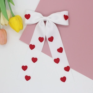 Detailed view of a white ribbon bow hair clip featuring 3D red heart embellishments