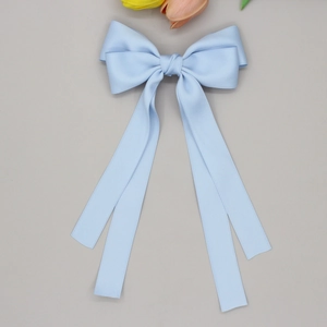 Détail d'une pince à cheveux avec ruban bleu clair et longs pans sur fond gris