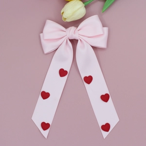 Détail d'une barrette à nœud rose avec des cœurs rouges en 3D et de longs rubans satin