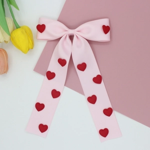 Detailed macro view of pink satin hair bow with red heart accents and long ribbons