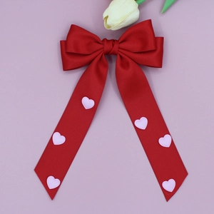 Détail d'une grande barrette nœud en soie rouge avec broderie de cœurs roses sur longs rubans