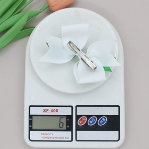 Close-up of lightweight white clover bow hair clip on a digital scale weighing 6 grams