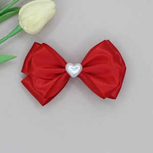Detail of red satin bow hair clip with a white heart-shaped pearl center decoration