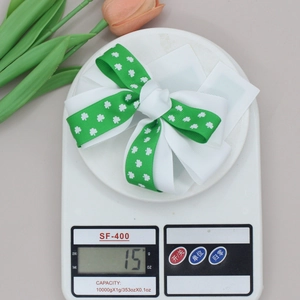 Detail showing the lightweight 15g weight of St. Patrick's Day clover bow hair clip on scale