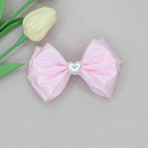 Detail of pink satin bow hair clip featuring a white heart-shaped faux pearl center