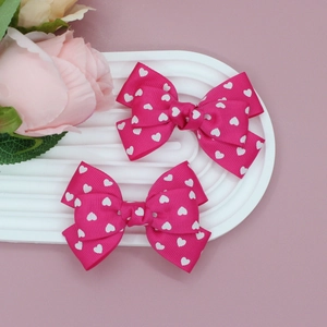 Détail de deux nœuds à cheveux rose foncé en gros-grain avec motifs cœurs sur un plateau