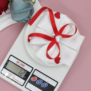 Barrette à cheveux avec nœud en soie et perle cœur sur fond rose avec décor floral