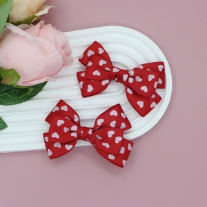 Détails d'une paire de barrettes à nœuds rouges avec motifs de cœurs blancs