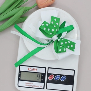 Close-up showing a 9g St. Patrick's Day clover bow clip on a digital scale for weight display