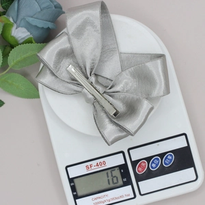 Silver-grey satin bow hair clip on a digital scale weighing exactly 16 grams