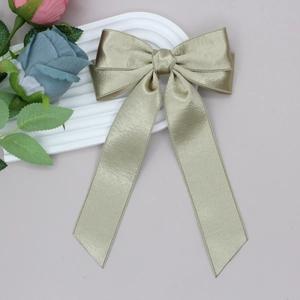 Detail of champagne satin bow hair clip with long ribbons on white textured tray