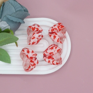 Close-up of two white grosgrain ribbon hair bows with red heart prints on a display tray