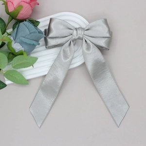 Silver-grey satin bow hair clip with long ribbons on a decorative white textured tray