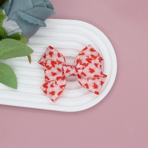 Macro detail of red and white heart print ribbon bow hair clip on elegant white dish