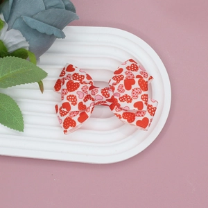 Close-up of handmade white grosgrain ribbon hair bow with red heart patterns on pink background