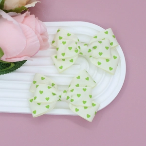 Détail de nœuds à cheveux en gros-grain crème avec motifs de cœurs verts sur un plateau