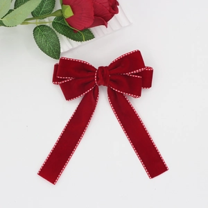 Detail of dark red velvet bow hair clip with white polka dot stitching and soft texture
