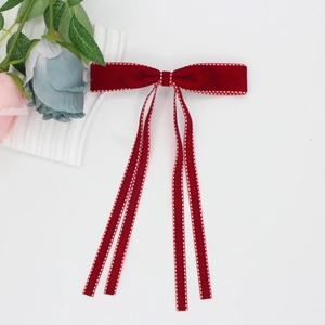 Detail of red velvet bow hair clip with white polka dot stitching and long streamers