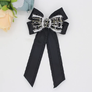 Detail of black bow hair clip featuring tweed fabric texture and long satin ribbons