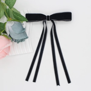 Detail of black velvet bow hair clip with white stitching and long elegant tassels