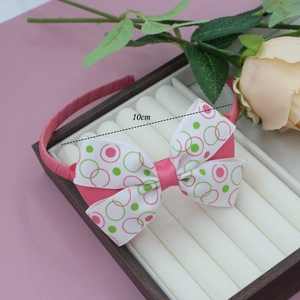 Détail d'un serre-tête en satin rose avec nœud de 10 cm sur plateau à bijoux