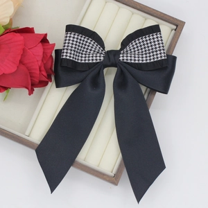Elegant black satin hair clip with houndstooth bow and long ribbons on a tray