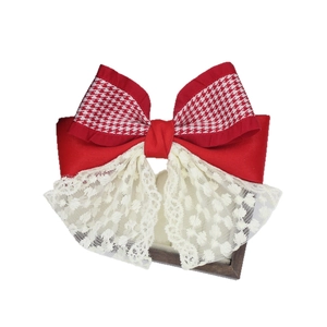 Red houndstooth ribbon bow hair clip with white lace trim on a wooden display stand