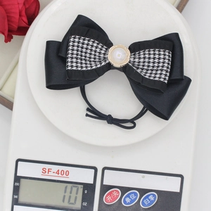 Detailed view of black and white houndstooth bow hair clip with pearl on digital scale