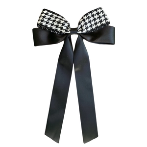 Detail of elegant houndstooth and black satin bow hairclip with long hanging ribbons