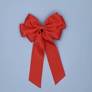 Detailed close-up of a large red satin bow hair clip with elegant long ribbon tails
