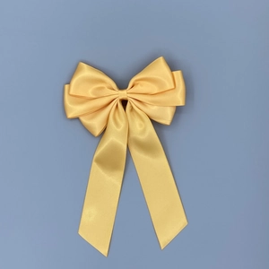 Detailed top view of a large yellow satin ribbon bow hair clip on a blue background