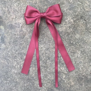 Détail d'une pince à cheveux nœud en satin bordeaux avec de longs rubans sur pierre