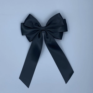 Close-up of black satin oversized bow hair clip with long ribbons on a blue-grey background