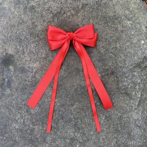 Gros plan d'un nœud à cheveux en satin rouge avec de longs rubans sur un fond de pierre