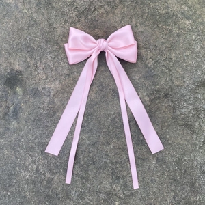 Vue détaillée d'un nœud à cheveux en satin rose avec de longs rubans sur fond de pierre