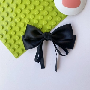 Close-up of elegant black satin bow hair clip with double layer and long silk ribbons
