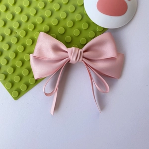 Detail of pink satin bow hair clip with elegant long ribbons and silk texture finish
