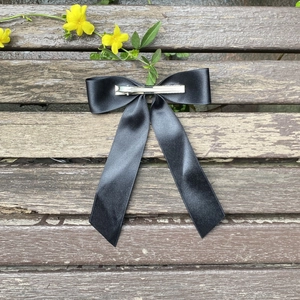 Elegant black satin ribbon bow hair clip with silver metal duckbill clip on wooden background