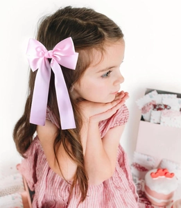 Detail of pink satin bow hair clip with long ribbons worn by a young girl